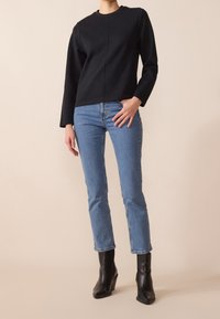 Haut noir à manches longues avec un col rond, associé à un jean droit bleu clair et des bottines à talons noires. Textures lisses sur l'ensemble.