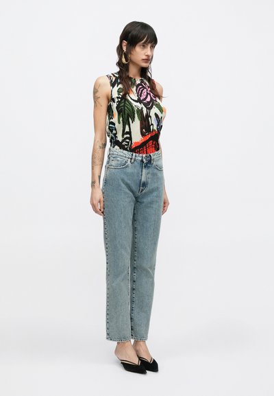 Πολύχρωμη αμάνικη μπλούζα με λουλουδένια και φυλλώδη σχέδια· ανοιχτό μπλε τζιν ψηλόμεσο· μαύρες γόβες με μυτερή μύτη· απλά αξεσουάρ.