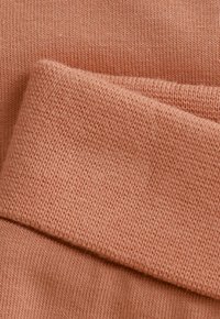 Zachte gebreide stof in een gedempte perzik kleur met een zichtbaar textielweefpatroon, weergegeven gevouwen over zichzelf.