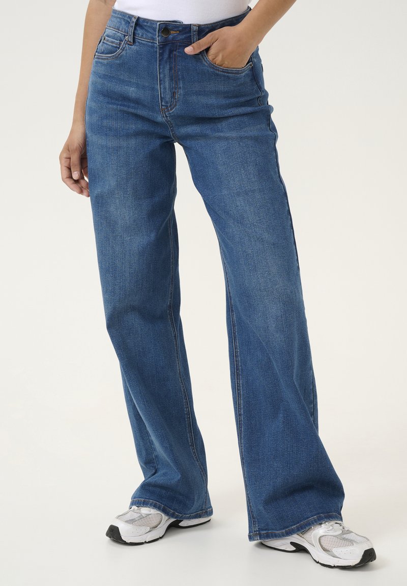 Jean en denim à jambes larges de couleur bleu moyen, doté de cinq poches et d'une taille haute, agrémenté de coutures contrastantes et d'accents en métal argenté.