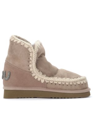 Botas tobilleras de ante beige con un borde trenzado crema, forro de piel suave y suela de goma texturizada. Presentan una marca metálica en el lateral.