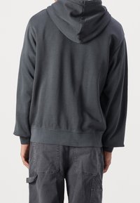 Felpa grigia con cappuccio, maniche lunghe e vestibilità ampia, realizzata in un tessuto testurizzato con orlo a coste. Vista posteriore mostrata.