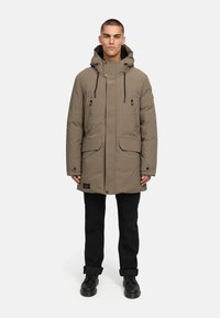Khaki parka bunda s kapucňou, ktorá má dve predné vrecká, čierne šnúrky a nášivku s logom na dolnom leme. Hladká textúrovaná látka.