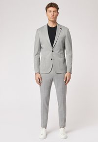 Lichtgrijs pak gemaakt van gladde stof met een jasje met twee knopen, notch-lapels en rechte broek, gecombineerd met witte sneakers.