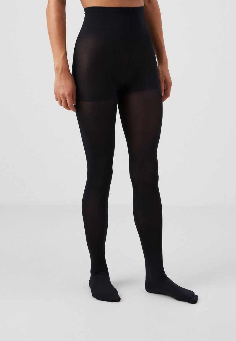 Collants noirs taille haute avec une texture lisse et transparente, présentant des jambes longues et une coupe ajustée, se terminant aux orteils.