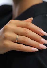 Goldener Bandring an einer Hand mit natürlicher, strukturierter Haut. Die Nägel sind lang und mandelförmig, lackiert in einem sanften Rosaton.