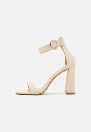 Beige højhælet sandal med firkantet tå, ankelrem og rund spænde. Fremstillet af glat syntetisk materiale; chunky hældesign.