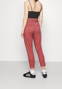 Roze tapered broek met elastische taille, zijzakken en details aan de achterkant, gecombineerd met zwarte sneakers en witte sokken.