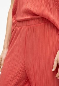 Plissé jumpsuit in koraalstof met een relaxte pasvorm, elastische tailleband en een gladde textuur, met een gelaagde top die over de broek valt.