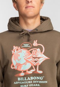 Brown hoodie featuring a graphic print of a globe and character with speech bubble. Text reads "Protect Your Playground." Material appears soft.