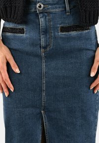Gonna a matita in denim blu scuro con spacco frontale, chiusura con bottone argento e dettagli neri testurizzati sulle tasche. Tessuto morbido e liscio.