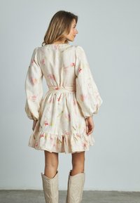 Helles, floral gemustertes Leinenkleid mit Puffärmeln, taillierter Taille und Rüsche am Saum, kombiniert mit dekorativen beigen Cowboystiefeln.