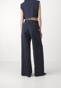 Marintrandig kort topp med hög krage och matchande vida byxor. Tyget är glatt med en subtil lyster och har en bakficka.