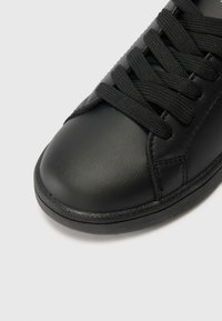 Basket en cuir noir avec un bout arrondi, surface texturée, lacets noirs et semelle en caoutchouc. Design minimaliste, sans détails de marque visibles.