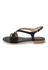 Black leather sandal with cross straps, flat sole, and a gold buckle. Features a smooth texture and brown sole accents. Simple design.