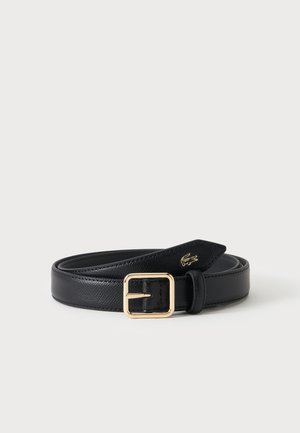 Ceinture en cuir noir texturé avec boucle carrée dorée et petit logo crocodile doré, enroulée sur une surface blanche.