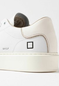 Sneaker bianco in pelle con tacco texturizzato, accenti chiari a contrasto, dettagli cuciti, logo quadrato nero e punta rotonda su una suola bianca.