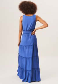 Blue maxi dress with sleeveless design, tiered ruffles, elastic waistband, and soft texture. Back view showing cinched waist and flowing skirt.