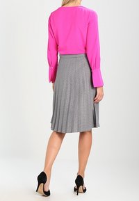 Fuchsiová blůza s dlouhými zvonovými rukávy; šedá skládací sukně s vzorem houndstooth; černé vysoké podpatky.