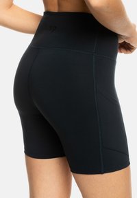 Svarte høye sykkelshorts laget av elastisk materiale, med flate sømmer og en liten logo bak for økt komfort.