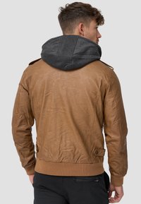 Veste en cuir marron avec une capuche en tissu gris, des poignets et un ourlet côtelés, et des épaulettes. Design ajusté et texturé avec des coutures apparentes.