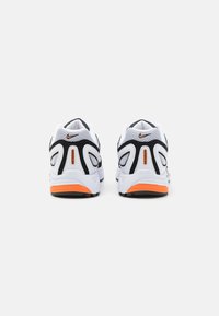 White and black athletic shoes with mesh texture, featuring orange accents on the sole and heel, and signature logo on the back.