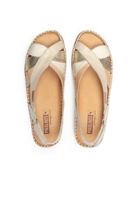 Sandalias de cuero con diseño de tiras cruzadas en beige y acentos metálicos. Bordes trenzados y una plantilla de cuero suave. Logo de la marca visible en el interior.