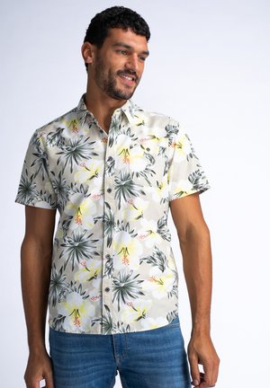 Camisa de manga corta con un fondo beige, presenta un patrón floral en amarillo y blanco, acentos en negro y un diseño clásico de botones.