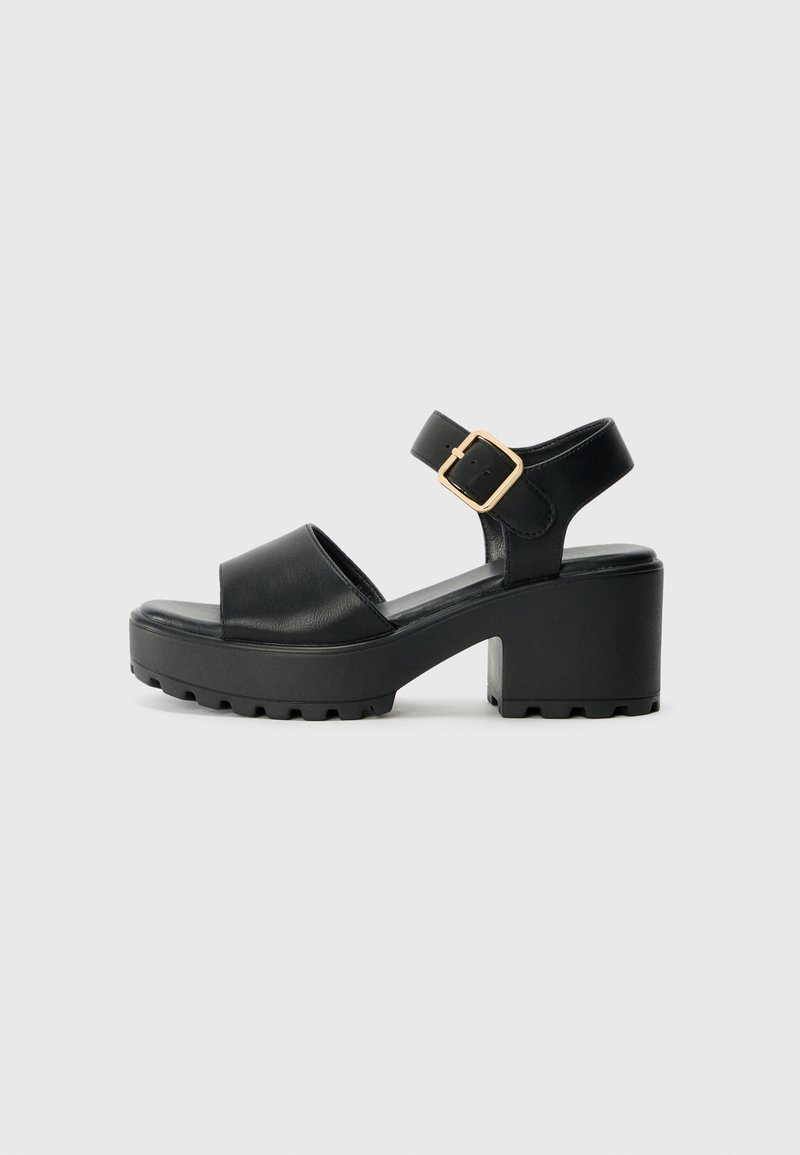 Schwarze Plattformsandalen mit einer glatten Lederoberfläche, breiter Vorderstrap, verstellbarem Knöchelriemen mit einer goldenen Schnalle und strukturiertem Sohlen.
