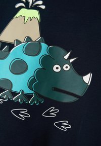 Grafica di un dinosauro blu su tessuto scuro con macchie circolari, un collare appuntito e un vulcano con lava, accentuata da impronte di dinosauro.