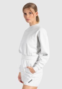 Witte sweatshirt en short set gemaakt van zacht materiaal. Beschikt over een relaxte pasvorm, ronde hals en elastische tailleband. Verzien van het "SMILODOX" logo.