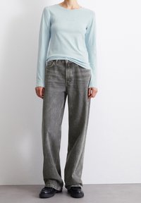 Vaaleansininen pitkähiha paita, jonka kanssa on väljät harmaat farkut ja mustat paksupohjaiset kengät. Minimalistinen muotoilu pehmeällä tekstuurilla.