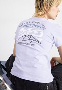 T-shirt in cotone lavanda chiaro con grafica di montagna, testo "Dickies Since 1922" sul retro, maniche corte e scollatura rotonda.