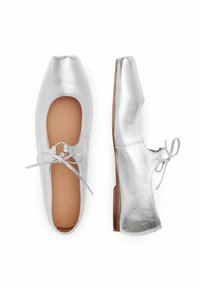 Bailarinas metálicas plateadas con punta cuadrada, lados expuestos y un lazo central. Presentan una plantilla color marrón y un tacón bajo marrón.