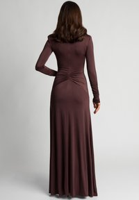 Długa, dopasowana brązowa sukienka z długim rękawem, z marszczeniami w talii i zwiewnym dołem, wykonana z gładkiego, elastycznego materiału.