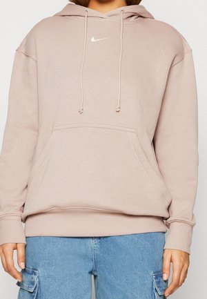Lichtbeige Nike-hoodie met voorzak en trekkoorden, gedragen met lichtblauwe denim cargobroeken.