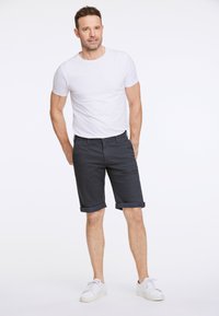 Pantaloni corti blu scuro con risvolti, abbinati a una T-shirt bianca aderente e scarpe da ginnastica bianche. Il tessuto sembra liscio e informale.