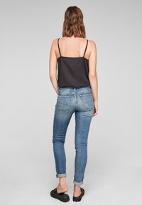 Svart ärmlös topp, blå denim skinny jeans med uppvikta anklar, och svarta slideskor. Slät tyg, figurnära design, avslappnad stil.