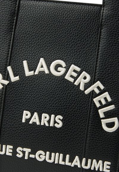 Черна текстурирана кожена повърхност с бял бродиран текст, гласящ "Karl Lagerfeld Paris Rue St-Guillaume."