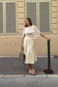 Kremowa sukienka z rozkloszowanym dołem i marszczeniami na ramionach. Dodatki to szara torebka i brązowe sandały.