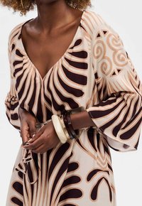 Vestido fluido con un estampado abstracto en tonos beige y marrón, escote en V y mangas sueltas. Los accesorios incluyen múltiples pulseras.