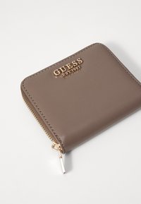 Portefeuille en simili cuir marron avec logo en doré "GUESS EST 1981", fermeture zippée et texture lisse. Design compact et rectangulaire.