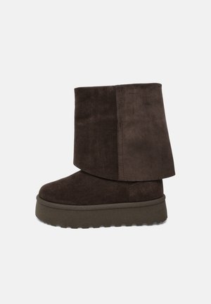 Botte mi-mollet en daim marron foncé avec revers replié et semelle épaisse en caoutchouc, vue de profil sur un fond uni.