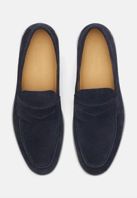 Mocassini in suede blu navy con una fascia frontale, dettagli cuciti e un'intersuola in pelle liscia color cuoio. Suola in gomma bianca.
