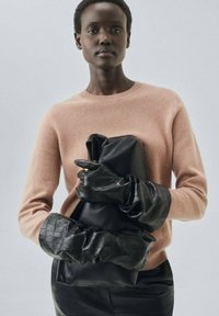 Roze kasjmier trui, zwarte leren handschoenen en tas, soepele texturen, overmaat ontwerp, verzameld materiaal met gouden hardware details.