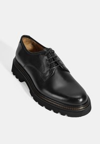 Chaussure noire en cuir à lacets avec un bout arrondi, surface texturée et semelle épaisse et chunky présentant des crampons proéminents et des coutures contrastées.