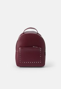 Sac à dos en cuir bordeaux avec une forme arrondie, fermeture éclair, poche avant ornée de petits clous en forme de cœur, et poignée supérieure pour le transport.