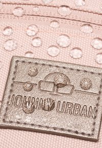 Pink fabric featuring raised water droplets, with a metallic tag embossed with "JOHNNY URBAN" and circular designs. Textured surface detail visible.