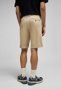 Beige Shorts aus glattem Stoff mit umgeschlagenen Säumen. Die Rückseite verfügt über zwei Taschen mit Knopfverschlüssen und einem Logodetail.