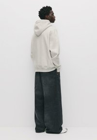 Felpa con cappuccio in cotone grigio chiaro, dal fit rilassato e polsini a costine, abbinata a jeans in denim scuri a vestibilità ampia con tasche posteriori.